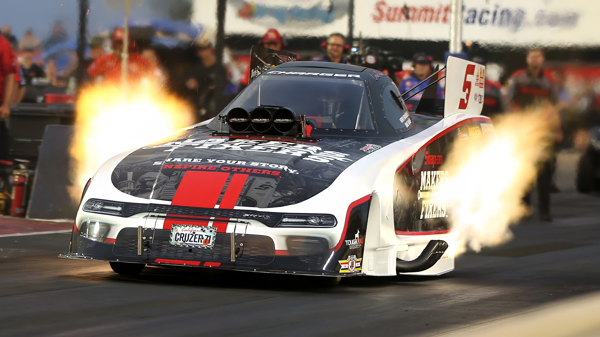 Drag racing car with flames bursting from exhaust pipes speeding down the race track.