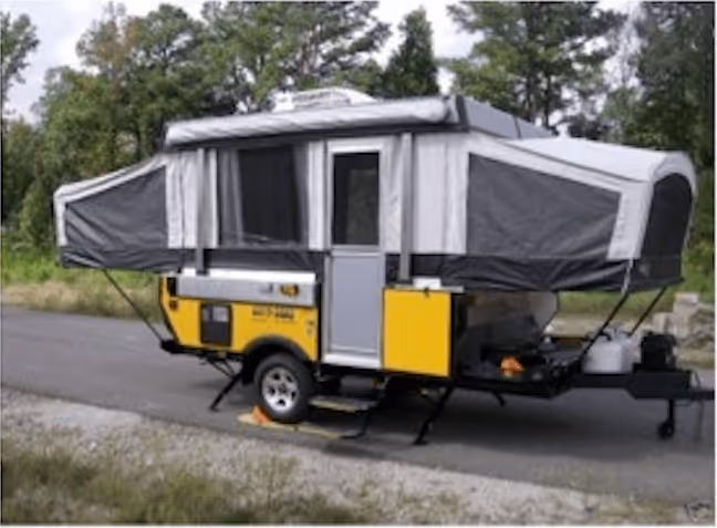 Yellow pop-up camper trailer with gray fabric sides set up on a roadside with trees in the background.