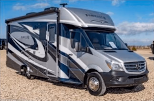 Silver and black Class C motorhome parked on gravel under a blue sky.