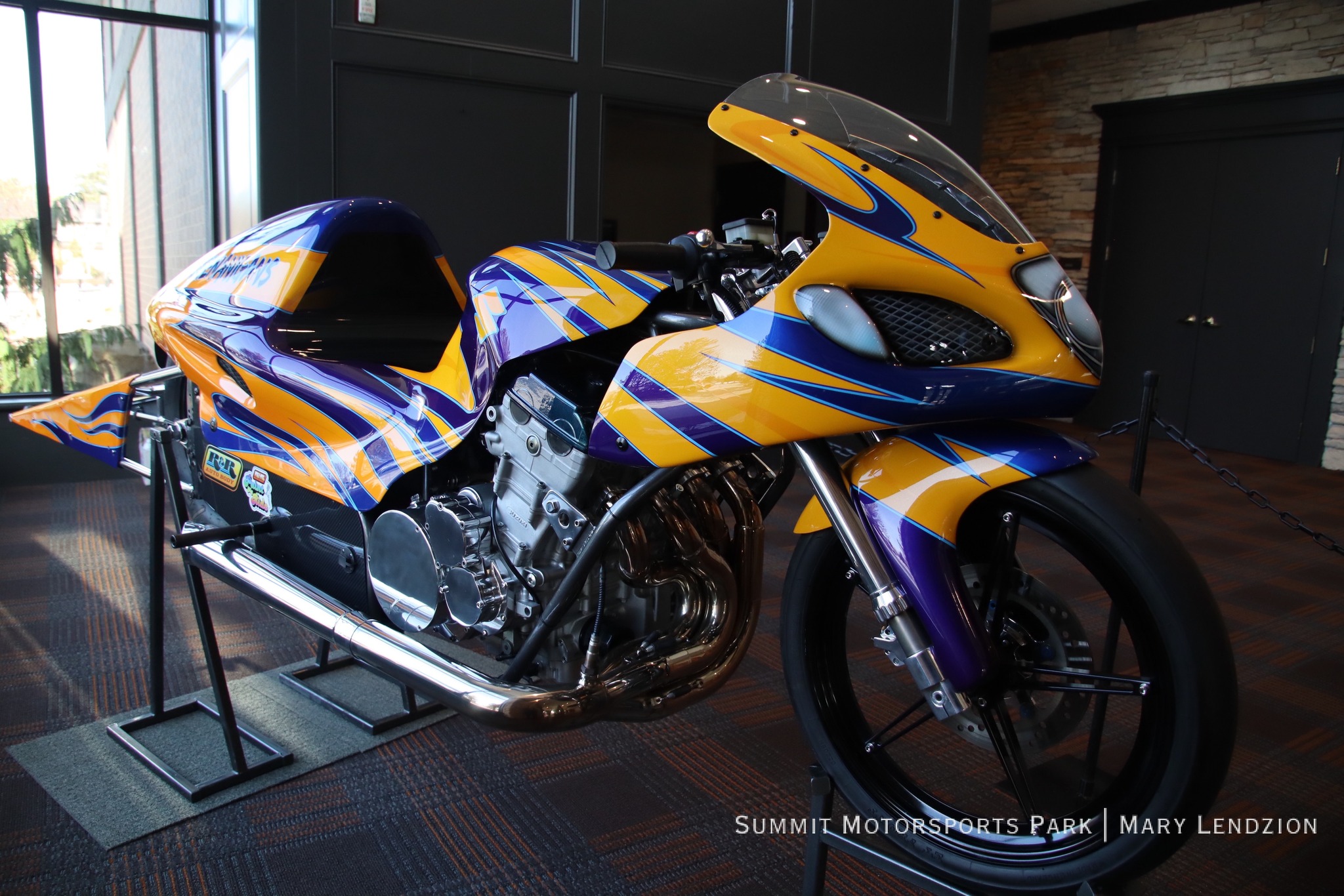 Yellow and purple racing motorcycle displayed indoors on a stand with a detailed engine and aerodynamic design.