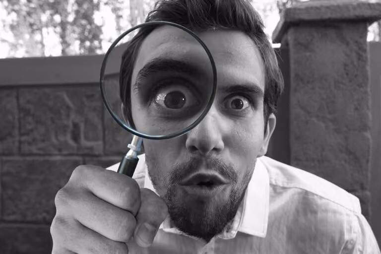 Man holding a magnifying glass up to one eye, making the eye appear enlarged and wide open.