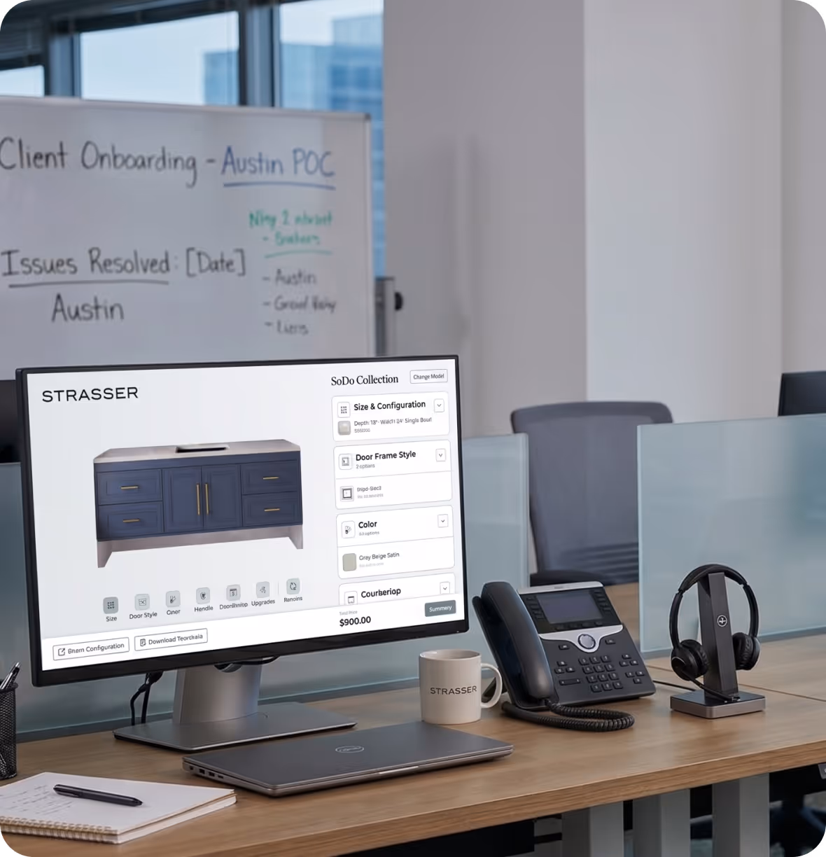 Office desk with computer showing STRASSER kitchen cabinet design app and phone, headset, and notebook.