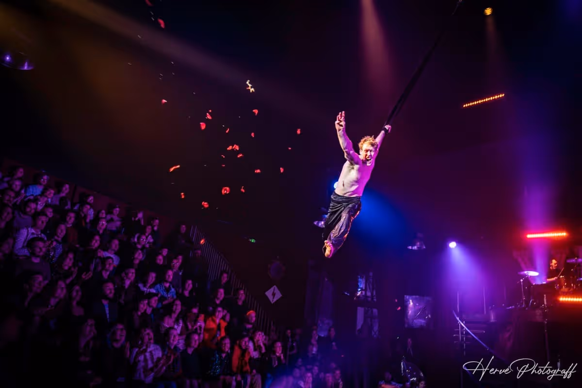 Acrobate suspendu en l’air au-dessus du public, entouré de confettis rouges.