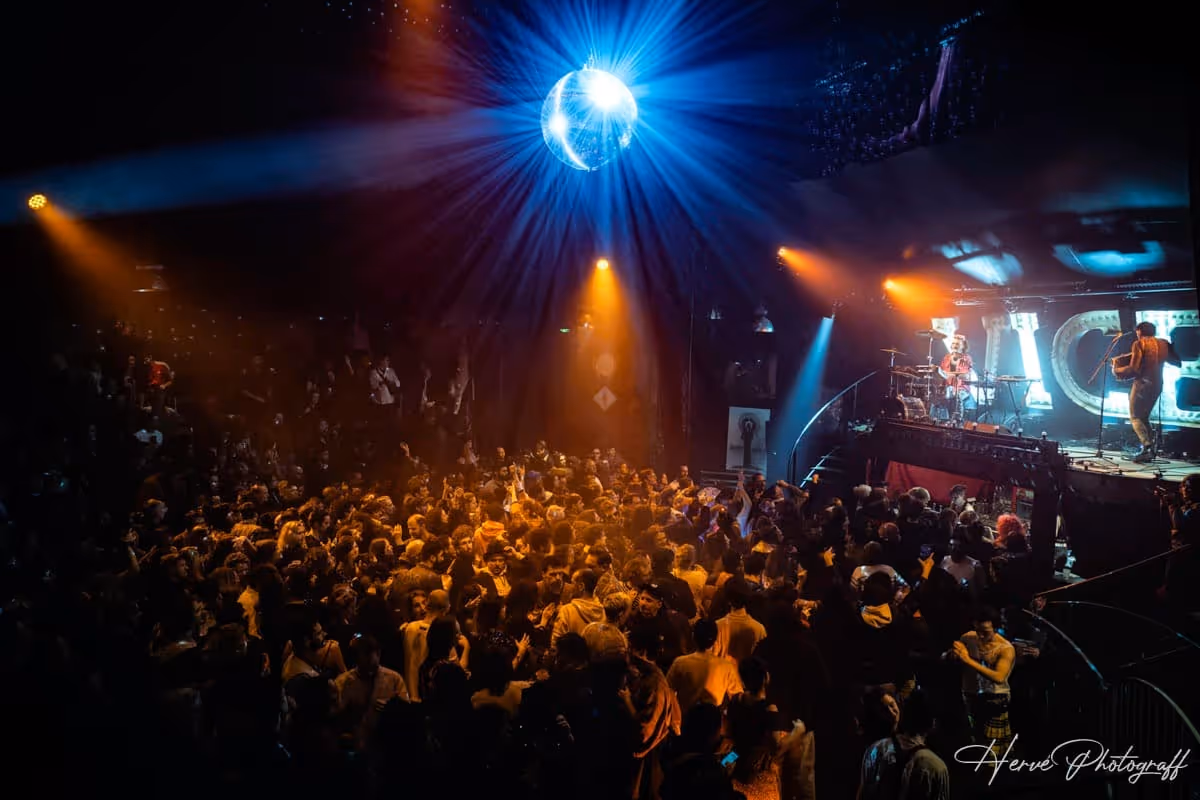 Salle remplie de spectateurs dansant sous une boule à facettes illuminée au Cabaret du Nouvel An.