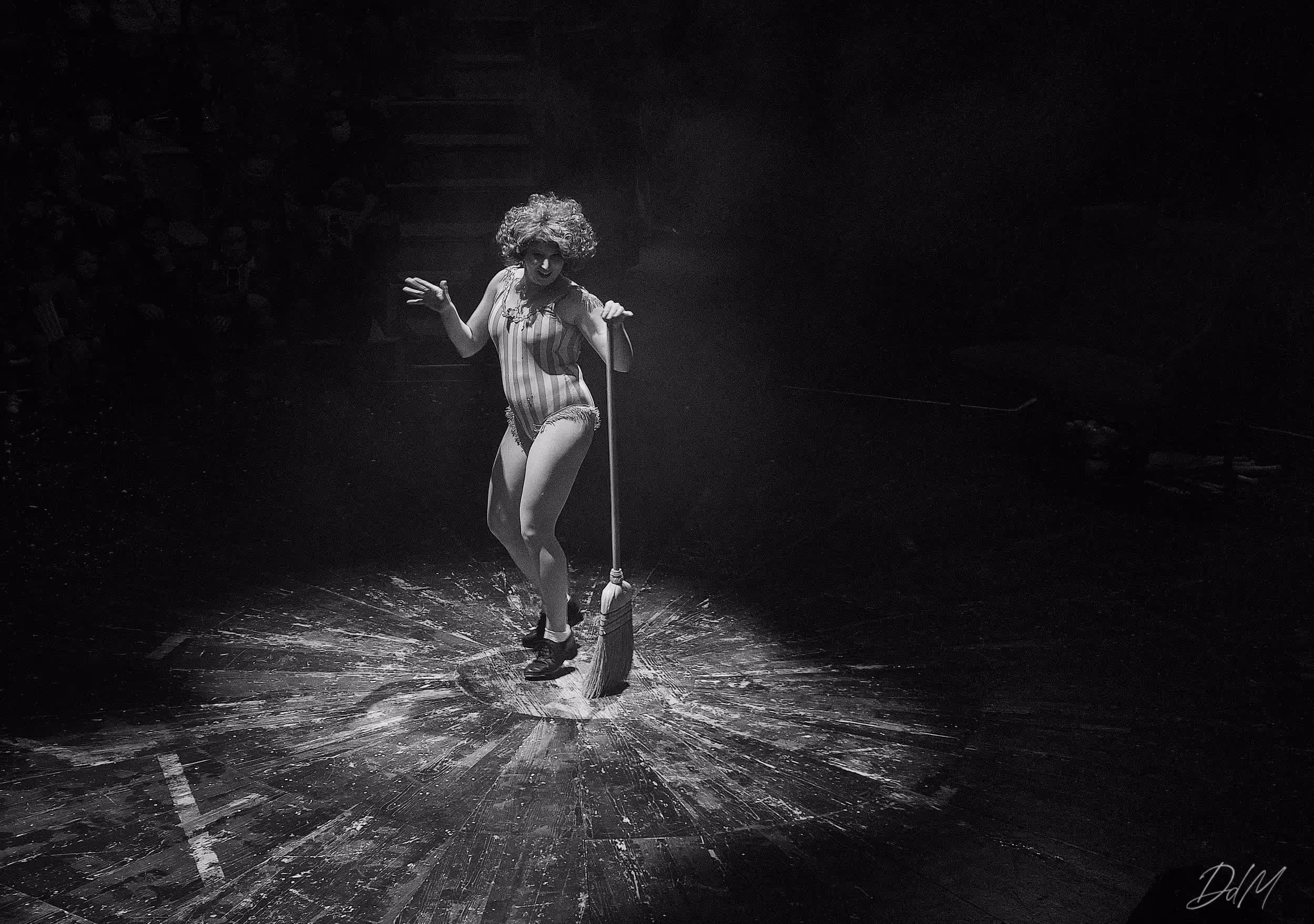 Artiste du Cirque Électrique en costume rayé, jouant un numéro clownesque sous un faisceau lumineux