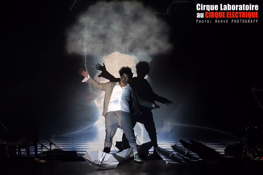 Cirque Électrique Laboratoire spectacle Paris - artiste en performance théâtrale, projections lumineuses, ombres dramatiques, mise en scène expérimentale, scénographie contemporaine, costumes blanc et gris, Hervé Photograff, arts visuels nocturnes