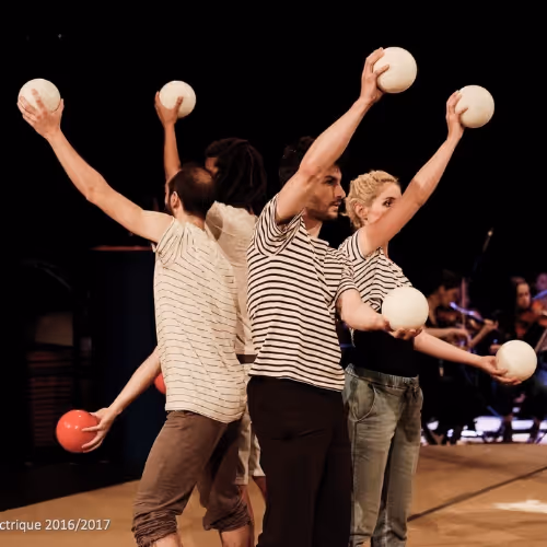 Quatre jongleurs sur scène portant des t-shirts à rayures, tenant des balles blanches et une balle rouge en position de lancer.