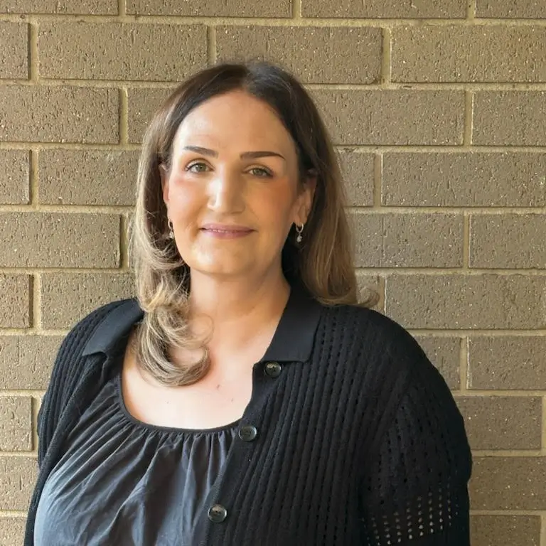 Woman in black top smiling in front of textured brick wall