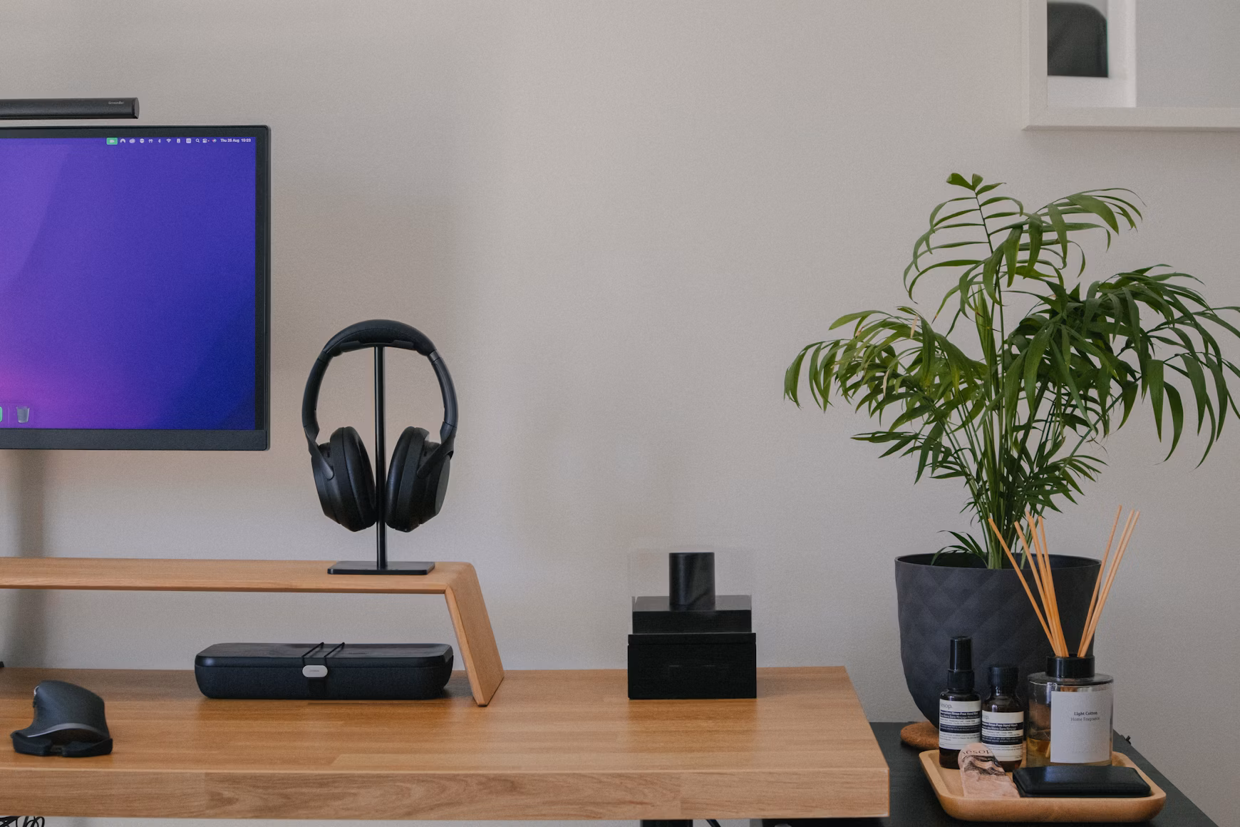 Minimalist wooden desk with black headphones on a stand, black storage case, a potted green plant, and a tray holding fragrance sticks and small bottles.