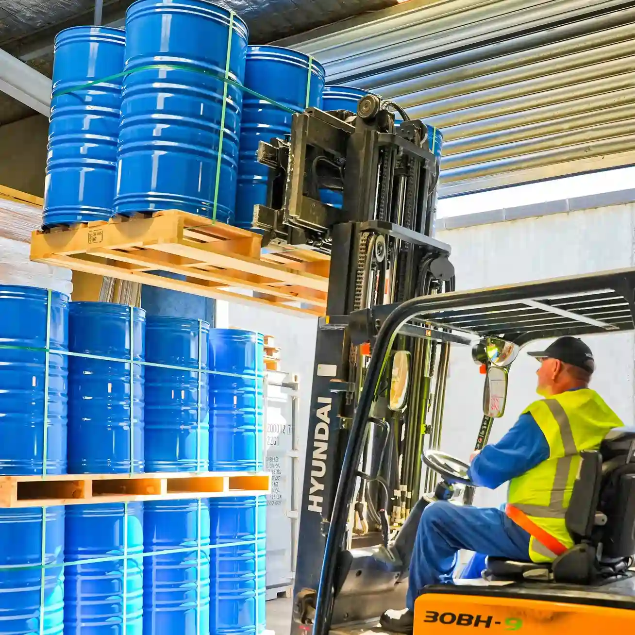 Man in forklift, removing pallet of blue drums from top stack