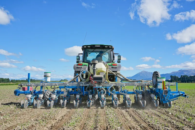 Tractor precision planting vegetable seeds with blue sky and mountains in the background