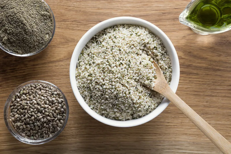 Hemp heart, hemp seed flour, hemp seed and hemp seed oil in bowls on wooden table
