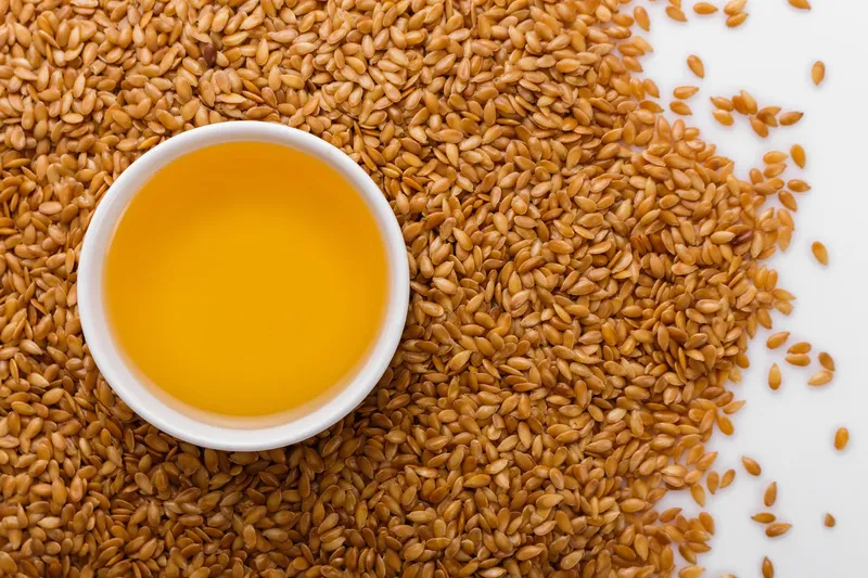 Golden linseed in a pile with small white bowl in middle with flaxseed oil
