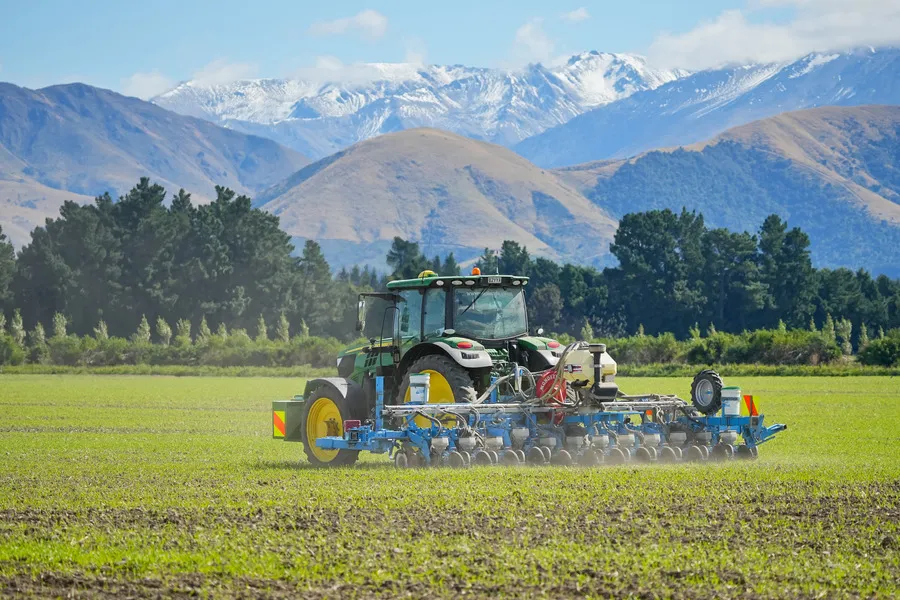 Tractor precision drilling high value seeds with blue sky and mountains in the background