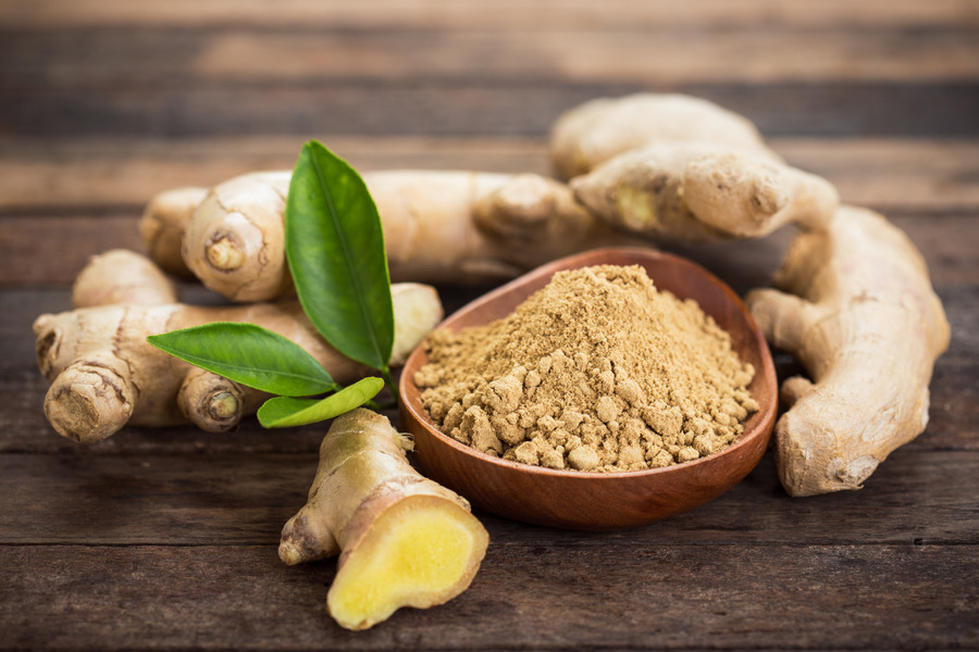 Ginger powder in wooden bowl surrounded but ginger