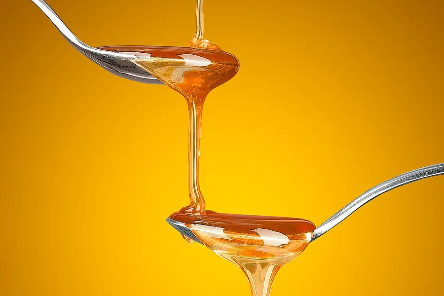 Honey falling from one spoon to another on a golden background 