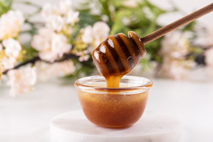 Wooden dipper stirring Manuka honey in small glass bowl