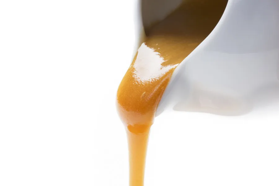 Manuka honey being poured from white sauce boat