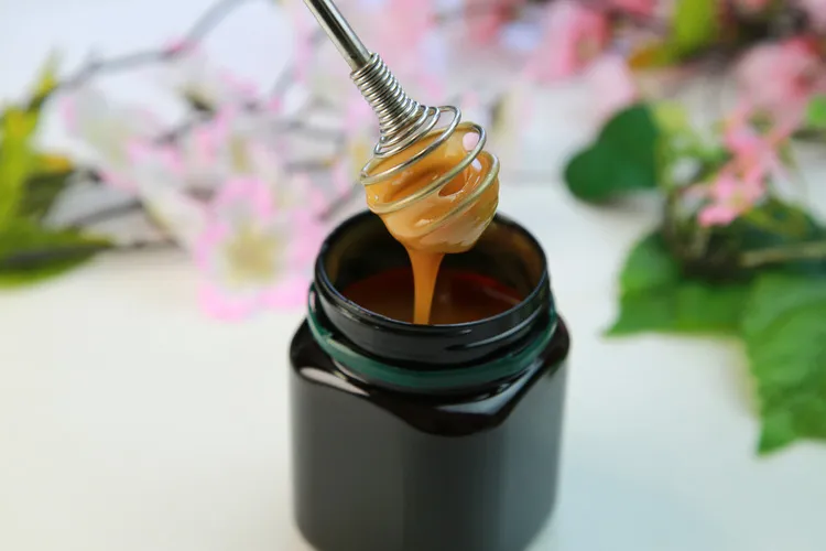 Manuka Honey in a brown square amber jar with metal honey stirrer