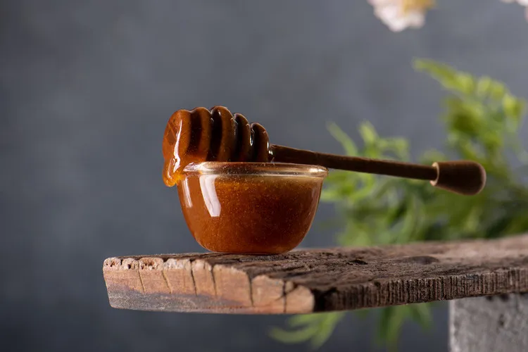 Manuka honey in glass bowl with wooden dipper sitting on top