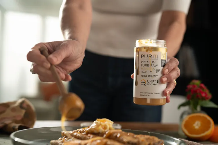 Women using wooden dipper to pour Puriti Manuka Honey onto crepes