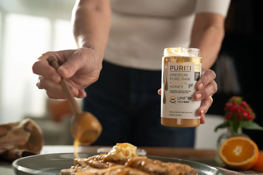Women using wooden dipper to pour Puriti Manuka Honey onto crepes