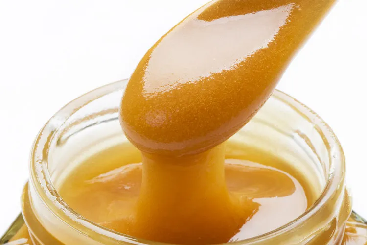Manuka honey on wooden spoon with a glass jar