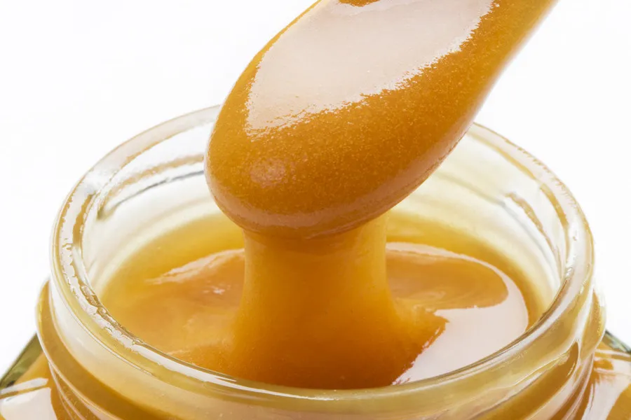 Manuka honey on wooden spoon with a glass jar