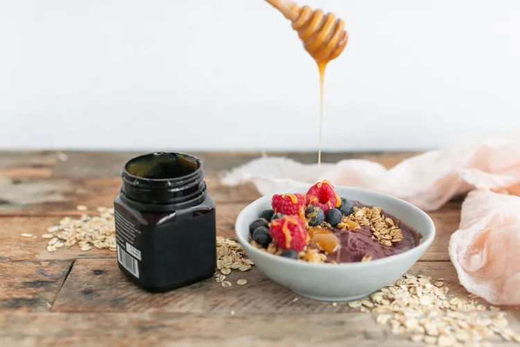 Manuka honey being dripped on breakfast cereal from wooden dipper