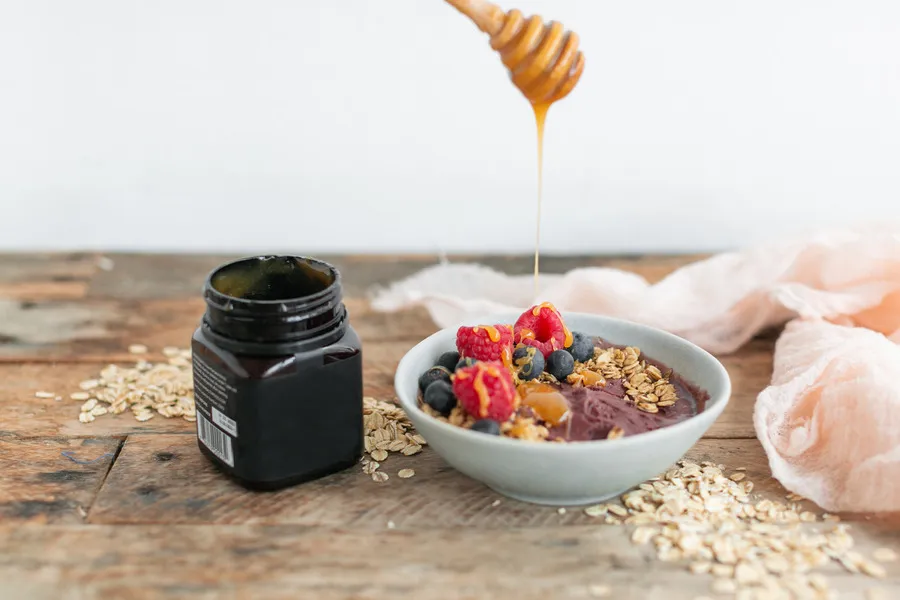 Manuka honey being dripped on breakfast cereal from wooden dipper
