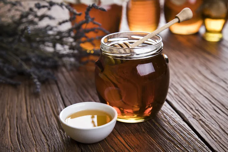 Thyme honey in glass jar with thyme flowers in background