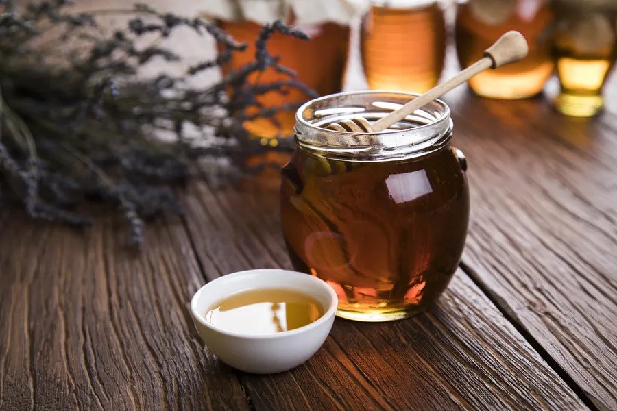 Thyme honey in glass jar with thyme flowers in background