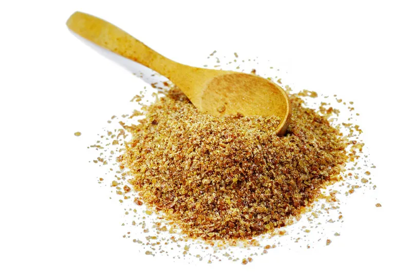 Ground Flaxseed in a pile with a wooden spoon on white background