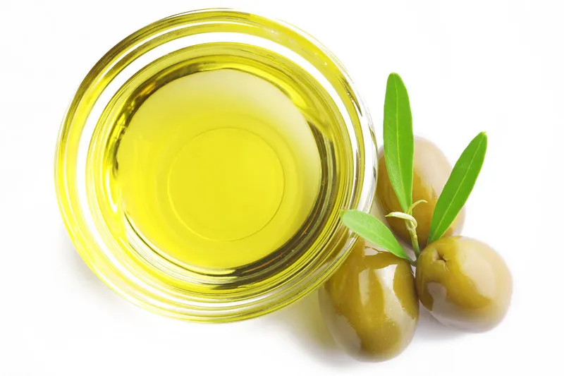 top down image of olive oil in small glass bowl with green olives on the side