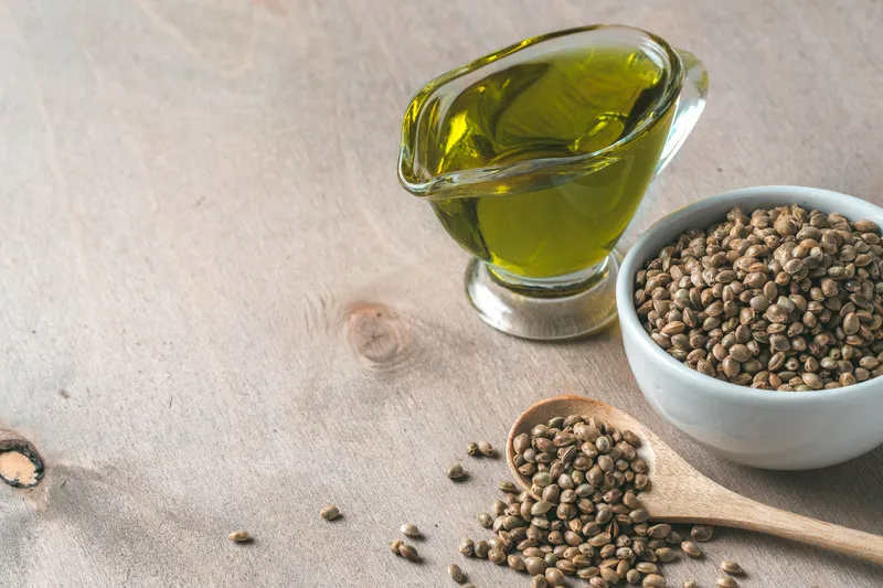 Hemp seed oil in glass jug with hemp seeds in white bowl beside it