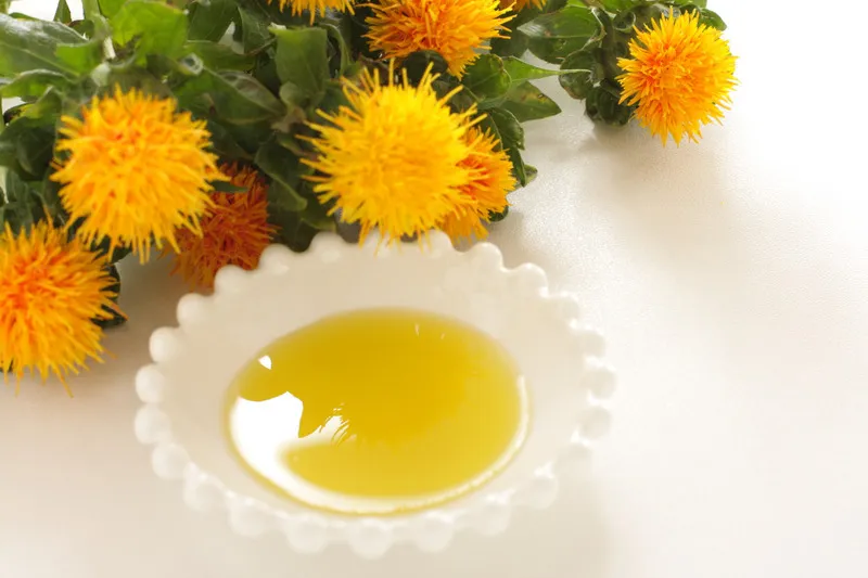Safflower oil in a small white bowl with yellow safflowers in background