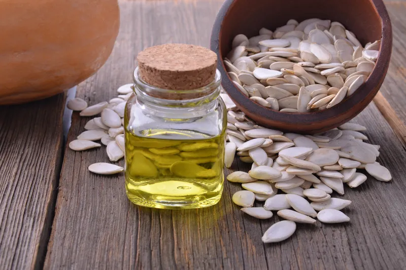 Pumpkin seed oil in glass jar with white pumpkin seeds in background