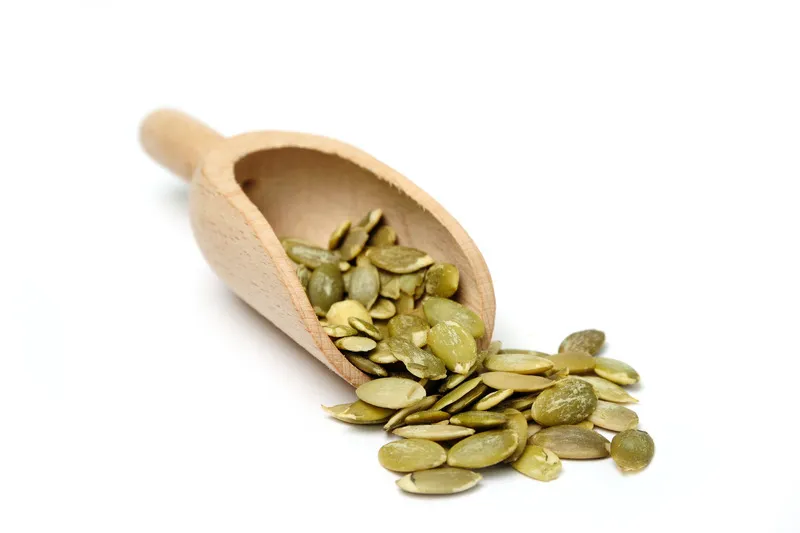 Green pumpkin seeds in a wooden scoop on a white background