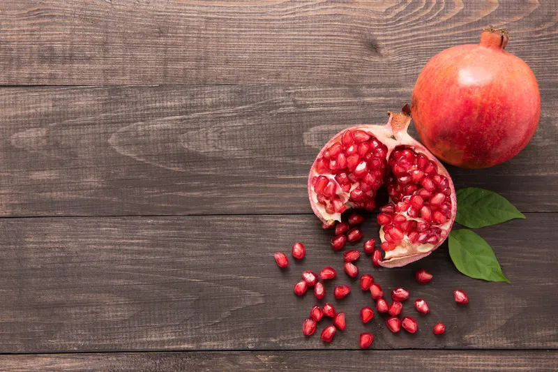 Two pomegranates, one whole the other cut with pomegranate seeds falling out
