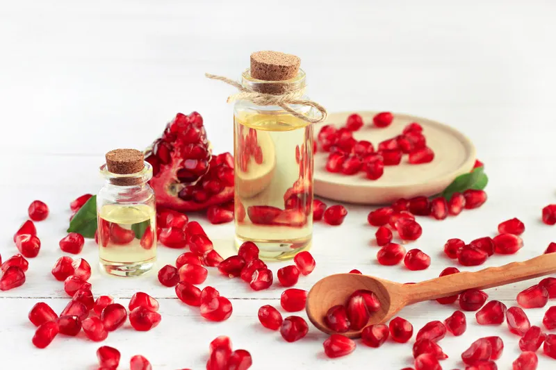 Pomegranate oil in small galss jar with pomegranate seeds in the background and foreground