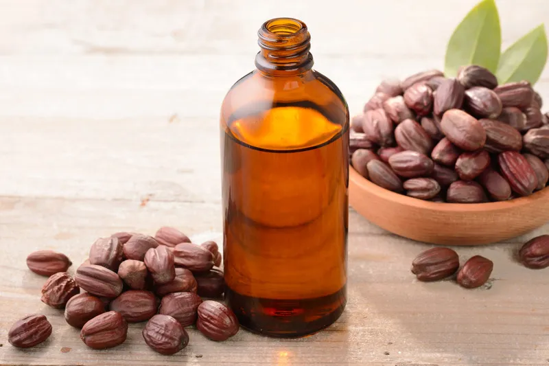 Jojoba oil in amber bottle with jojoba pods in wooden bowl in the background