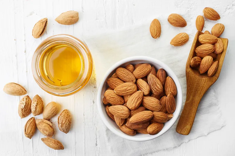 Top down shot of almond oil in a small glass jar with almonds in a small white bowl