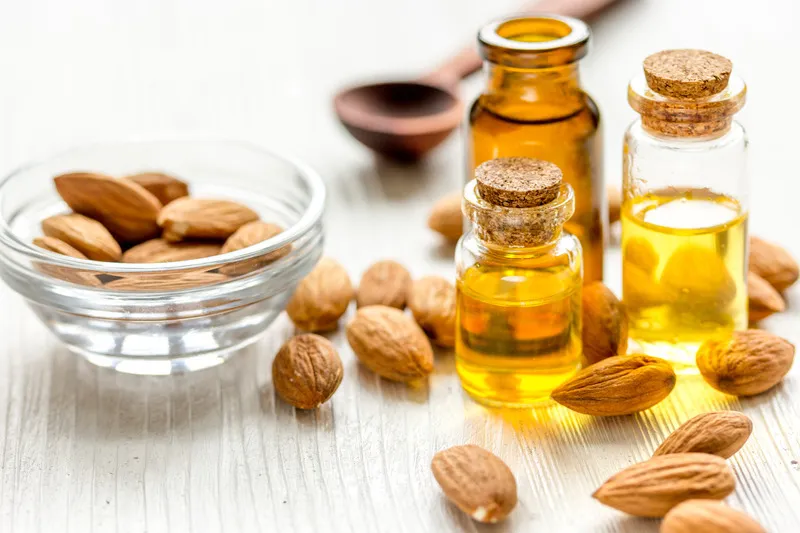 Apricot kernel oil in three small glass bottles with apricot kernels surrounding them
