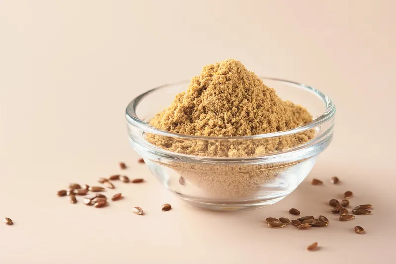 Flaxseed fibre in small glass bowl with flaxseed surrounding it