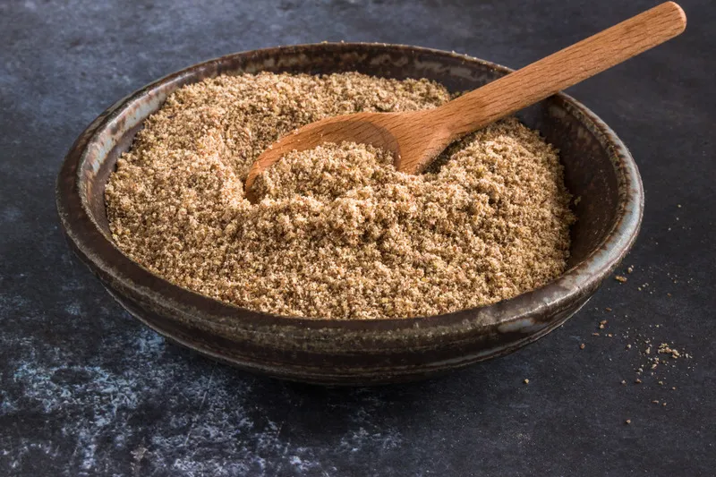 Ground flaxseed in bowl with wooden spoon