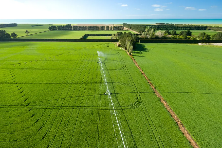 Aerial shot of a green flaxseed crop with an irrigation and the Pacific Ocean in the background