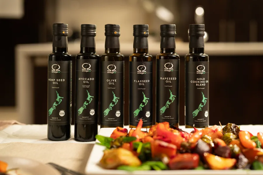 OmegaNZ bottled oil range sitting on a table behind roast vegetable salad