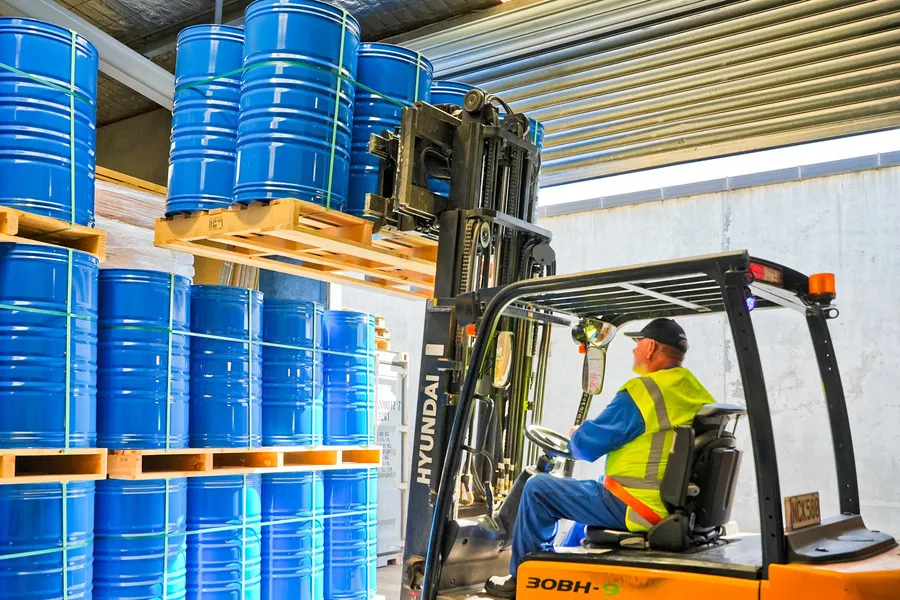 Man in forklift, removing pallet of blue drums from top stack