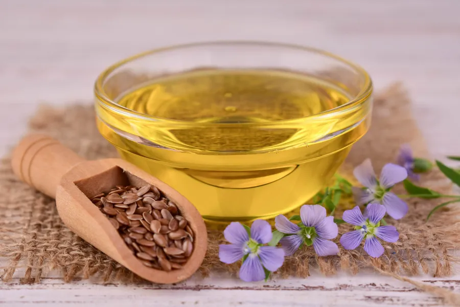 Flaxseed oil in a glass bowl with purple flaxseed flowers and flaxseeds