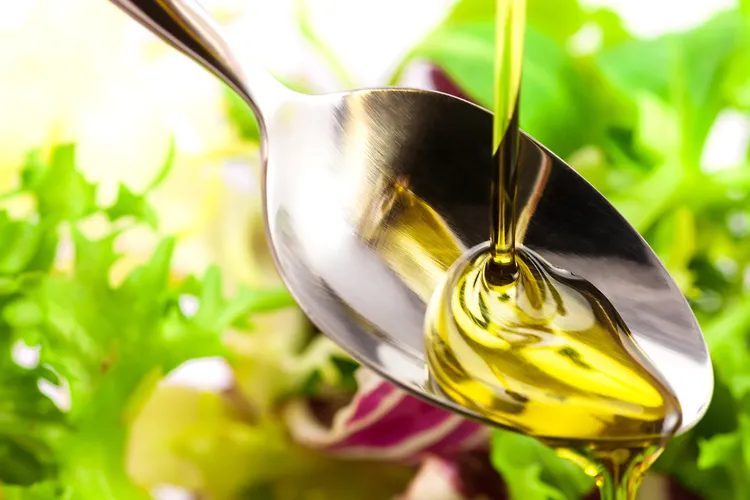 Golden flaxseed oil being poured onto a spoon with a green salad in the background